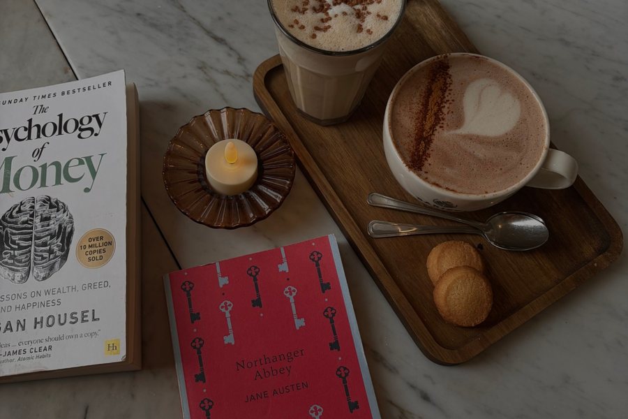Two lattes on a wooden tray beside Northanger Abbey on a marble café table