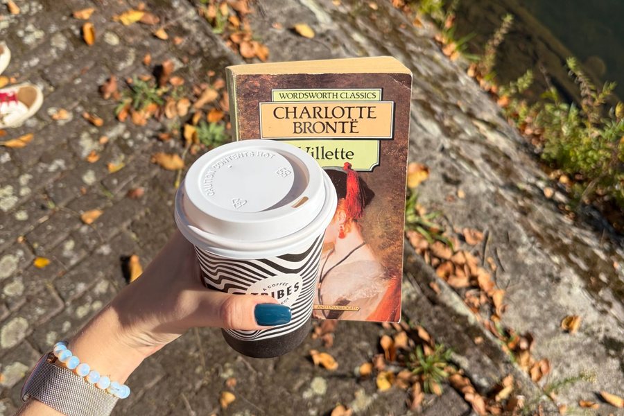 A takeaway coffee held up next to a copy of Villette by Charlotte Brontë
