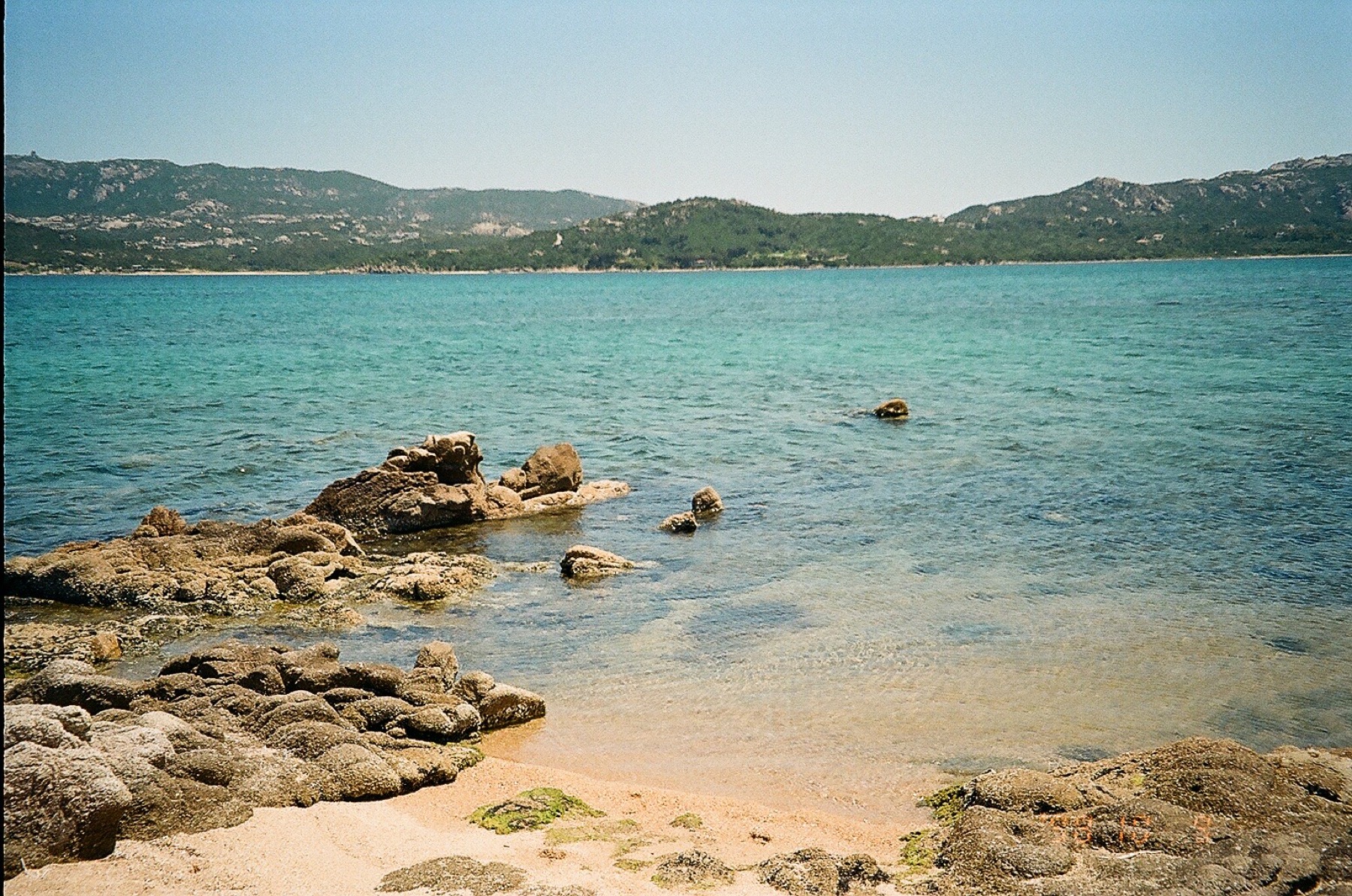 A quiet rocky cove with calm turquoise water, shot on film